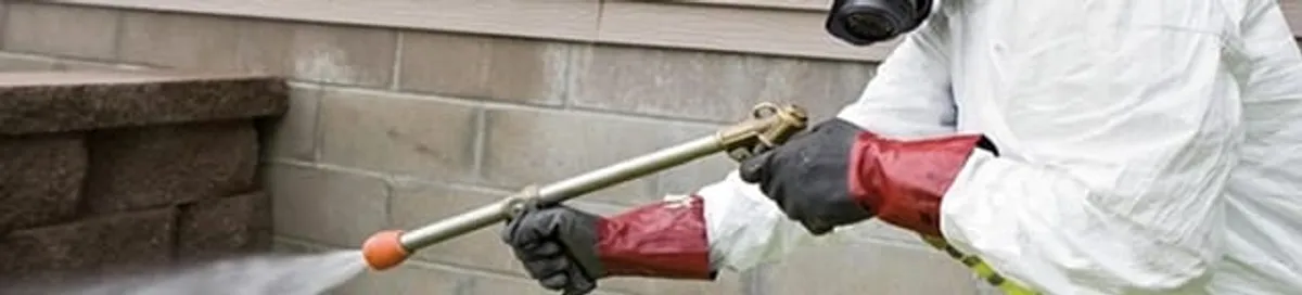 Pest control technician applying exterior insect treatment along a home foundation in Jackson, MS