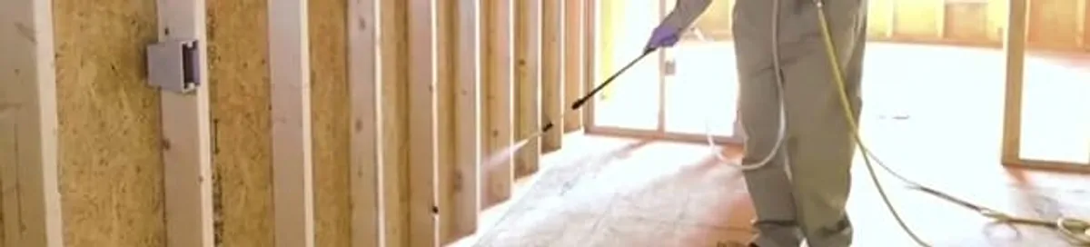 Termite treatment technician applying spray along framing and unfinished walls in Jackson, MS