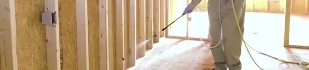 Termite treatment technician applying spray along framing and unfinished walls in Jackson, MS